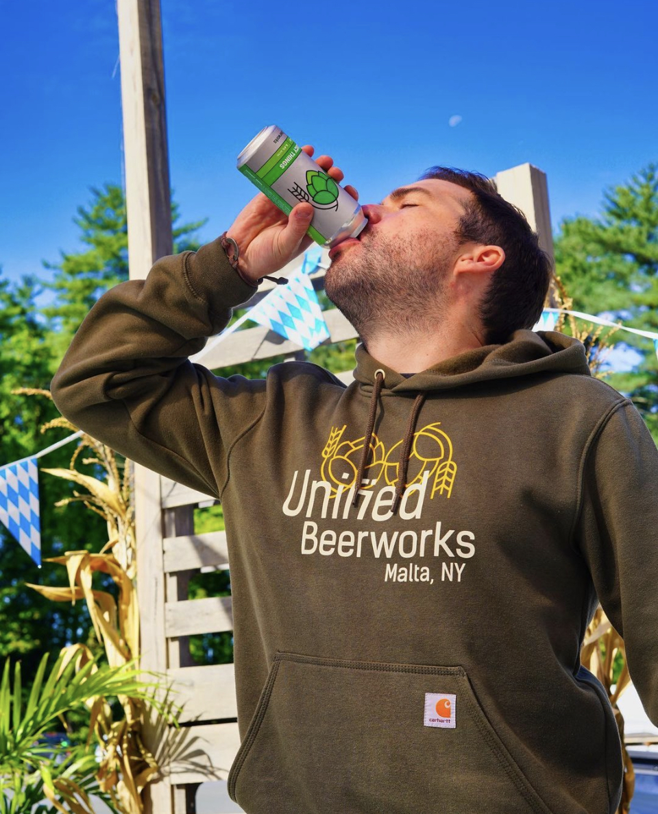 Man drinking a beer wearing a Unified sweatshirt